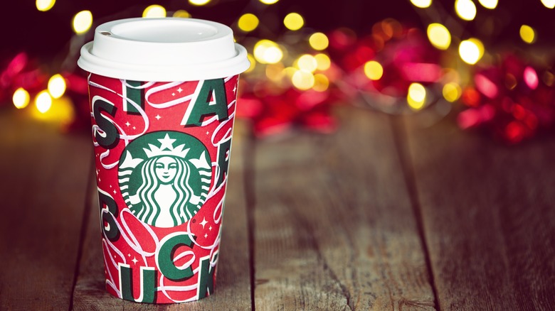 Starbucks holiday cup on wooden table with lights in background