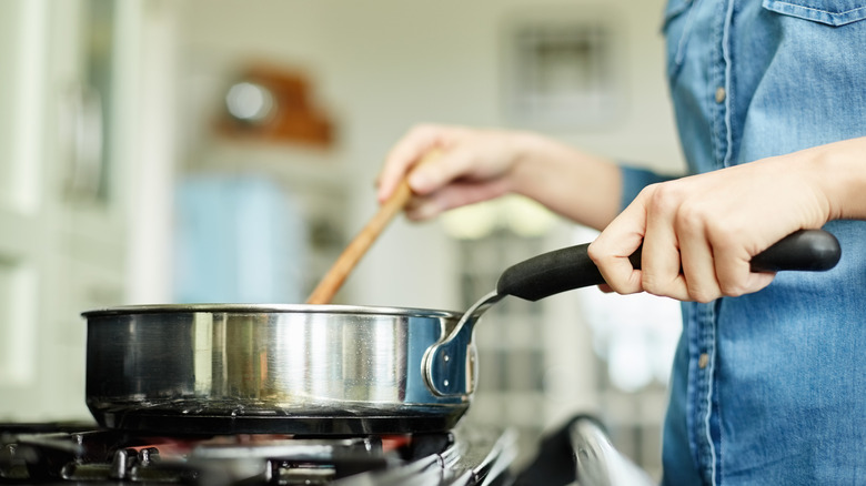 person stirring saucepan on stove