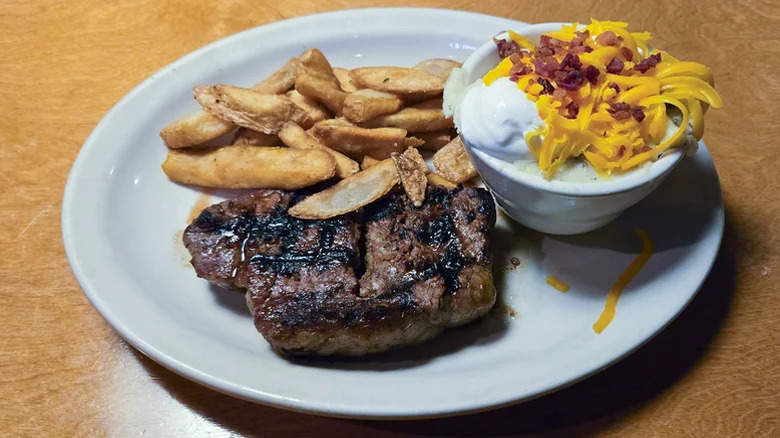 A New york Strip steak on a plate with fries and sauce.