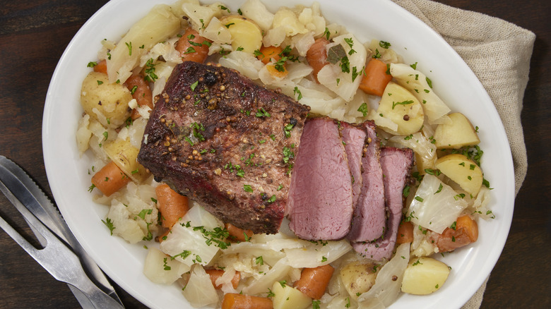 Corned beef surrounded by cabbage, carrots, and potatoes on a plate