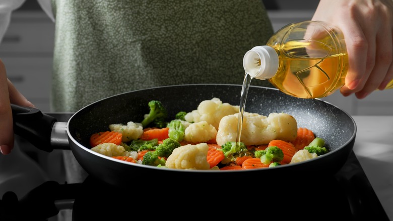 Person pouring oil into pan of veggies