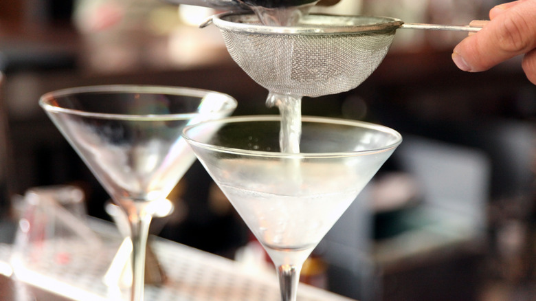 Bartender pouring martinis into chilled glasses 