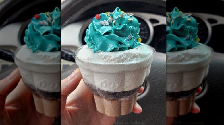 Person holding a Dairy Queen cupcake with blue frosting and sprinkles
