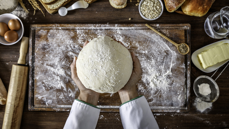 Hands holding rounded dough over a floured cutting board