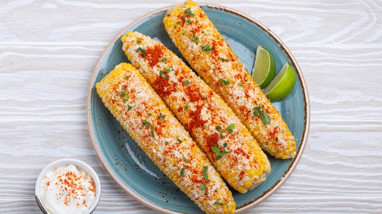 Elote on the cob with lime wedges on plate