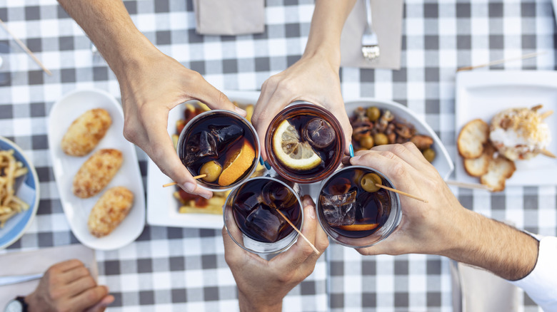 Four hands holding glasses of vermouth over table