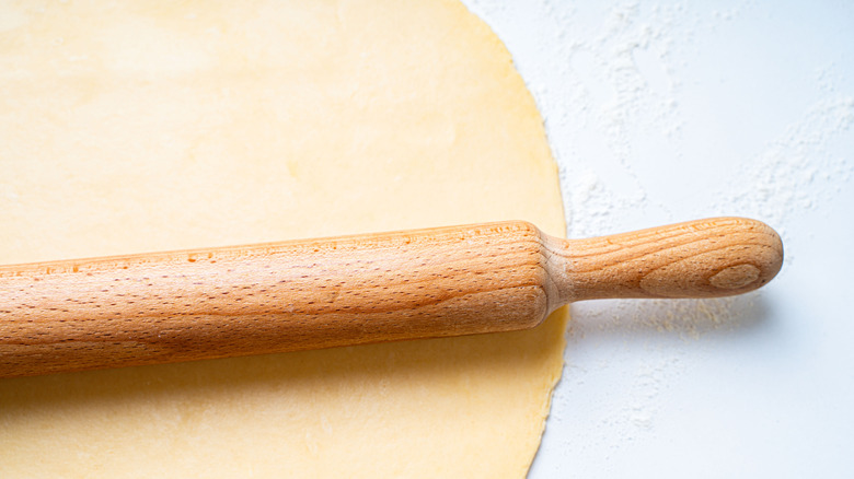Rolling pin rolling out raw dough on counter