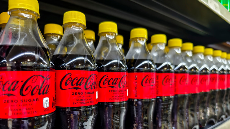 Shelf of Coca Cola bottles with yellow caps