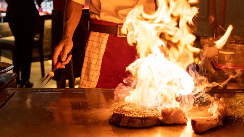 A hibachi chef flambeing a steak