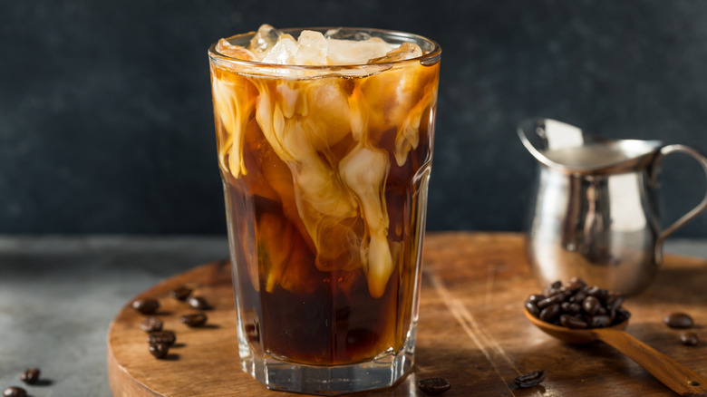 Glass of iced coffee with oat milk on wooden board