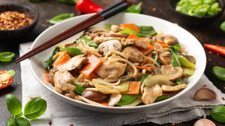 Chop suey in a white bowl with chopsticks