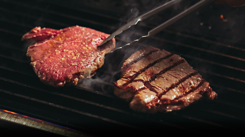Tongs flipping steak on a grill