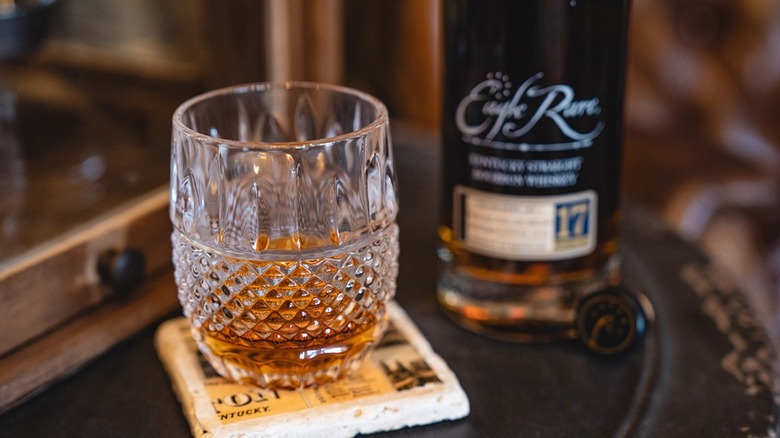 A glass of bourbon with a blurred bottle in Eagle Rare 17 in the background