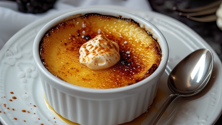 crème brûlée topped with whipped cream and cinnamon in a ramekin on a plate