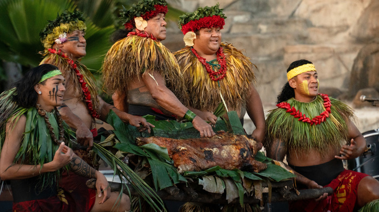 Hawaiian people in traditional clothing present a kalua pig