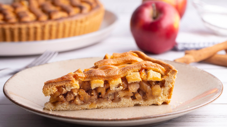 Apple pie slice on plate with apples in background