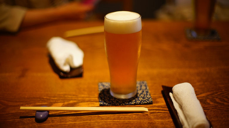 A single glass of beer on a table with chopsticks.