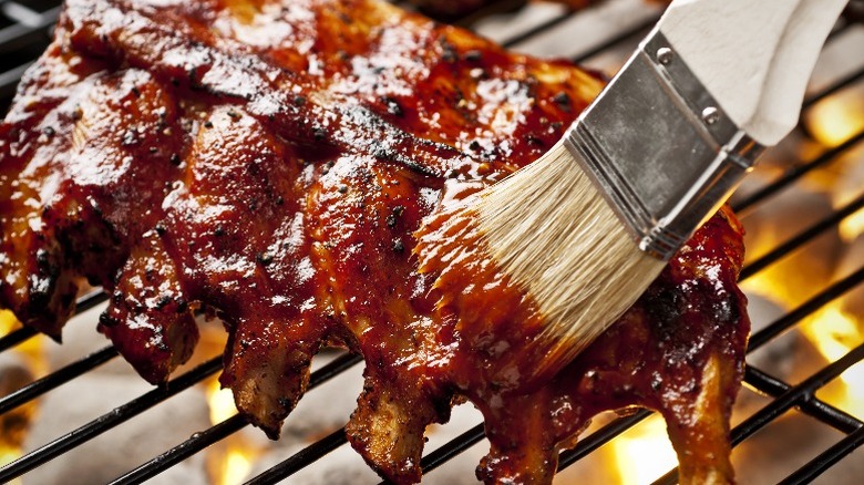 Some barbecue sauce is brushed on pork ribs on a grill.