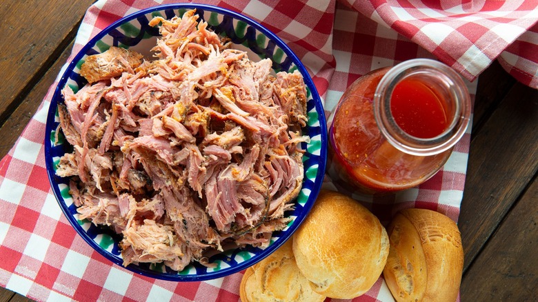 Pulled pork with barbecue sauce and bread sit on a checkered cloth.