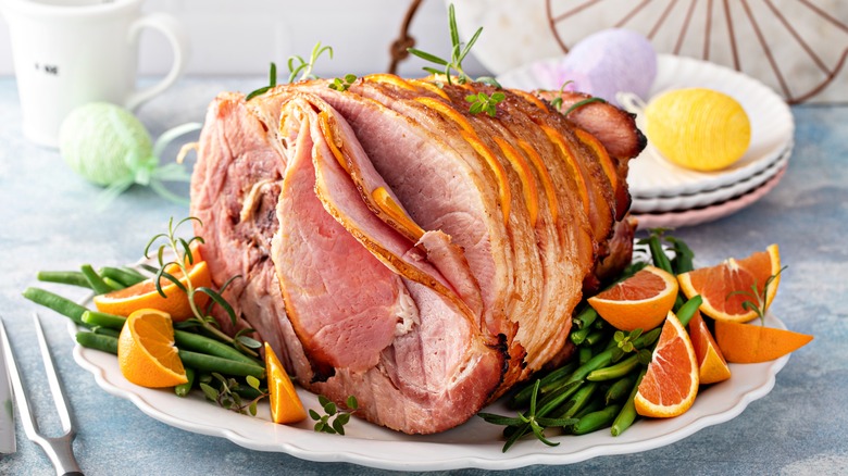 A baked ham with oranges and green beans