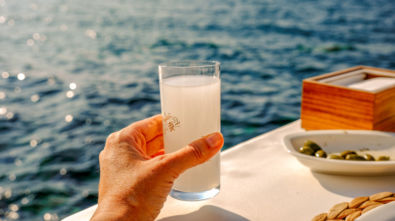 glass of ouzo held in hand with green olives