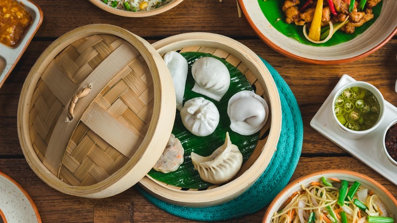 Dim sum steamer basket with variety of dumplings surrounded by other Chinese dishes