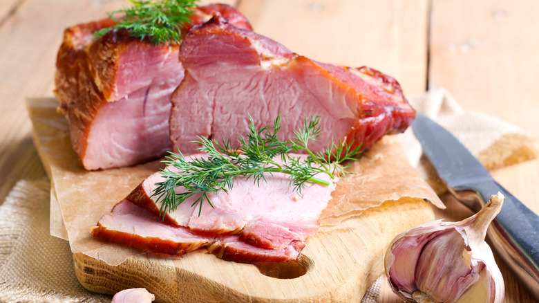 Sliced, smoked country ham on a cutting board with fresh herbs