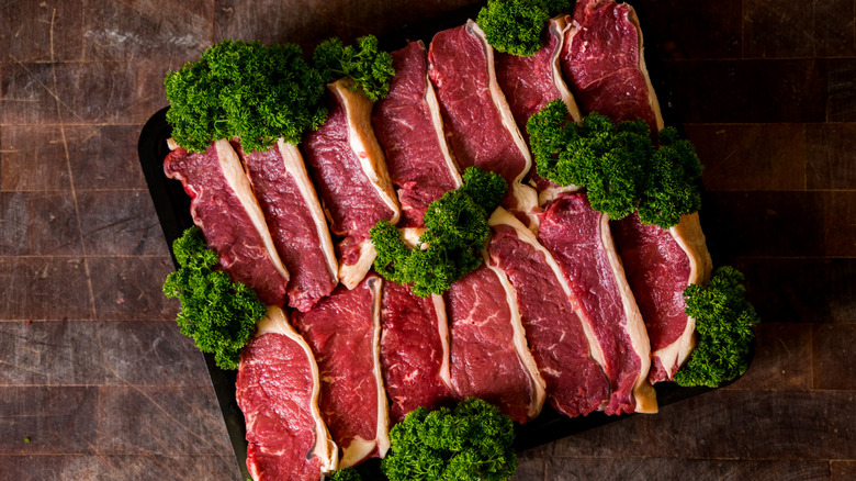 Cuts of grass-fed steak sit on a black tray surrounded by parsley