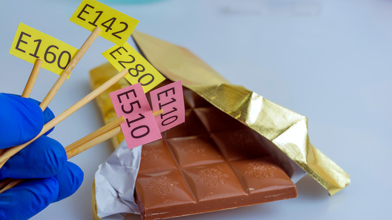 Person holding additive "E numbers" next to chocolate bar