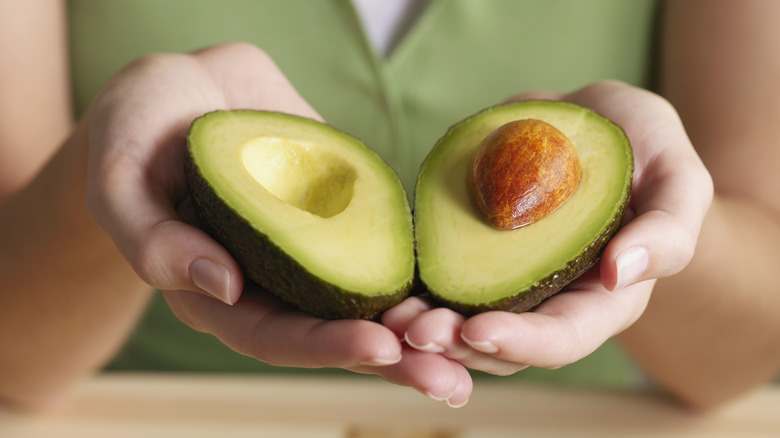 A woman holding a split avocado