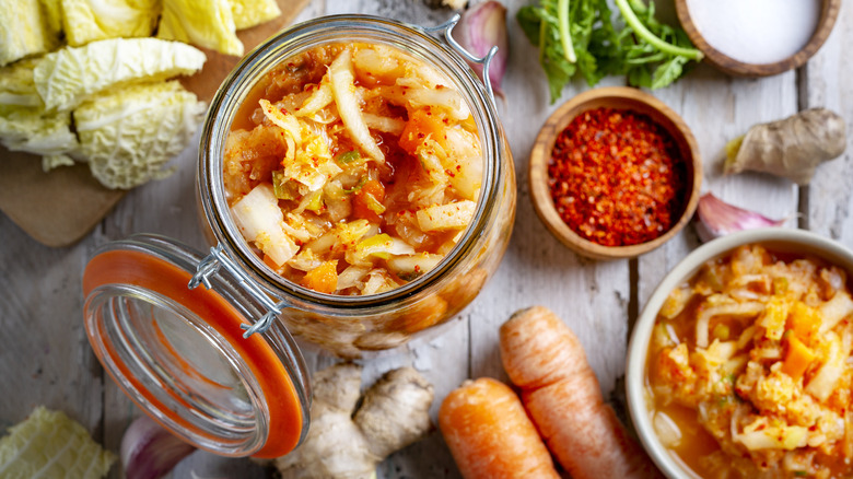 Kimchi in a jar next to ingredients like cabbage and carrots