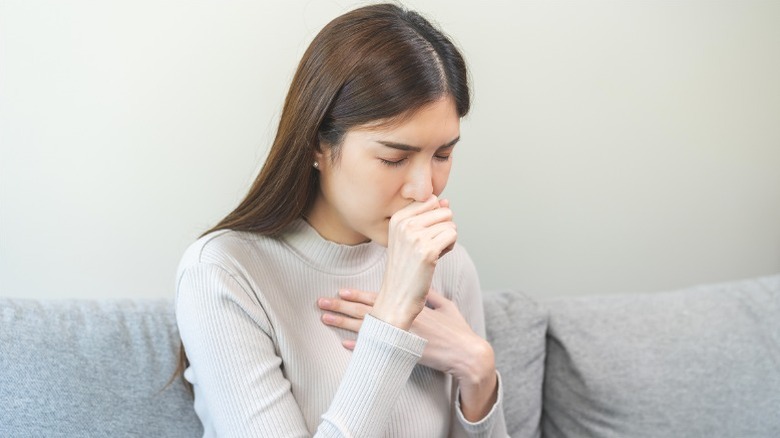 Woman covering mouth to cough, hand on chest.