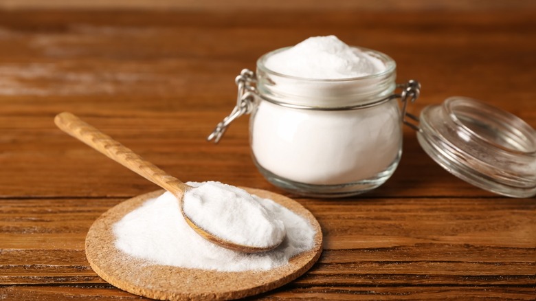 A pile of baking soda under a wooden spoon next to a jar of baking soda