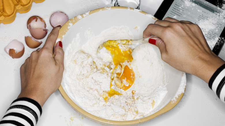 Messy cake ingredients in a bowl as a person stirs.