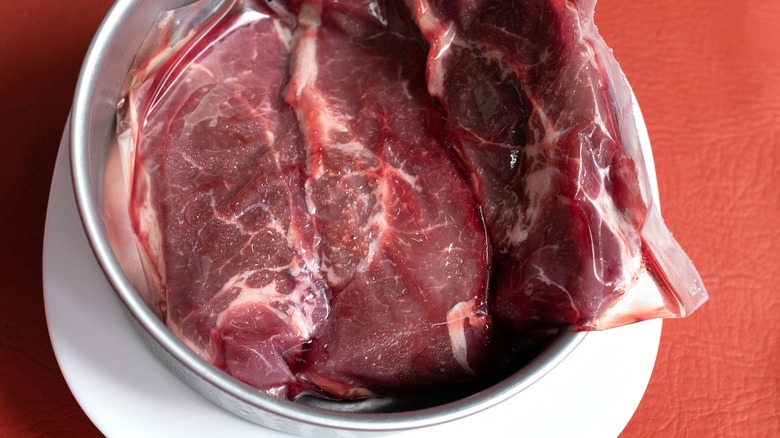 Steaks in a plastic bag in a pot ready for defrosting