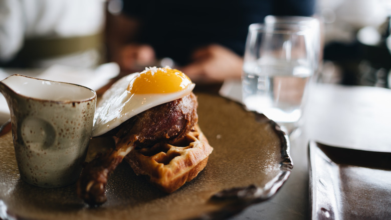 A sunny side up egg atop a roasted duck leg, egg, and waffle at Duck & Waffle