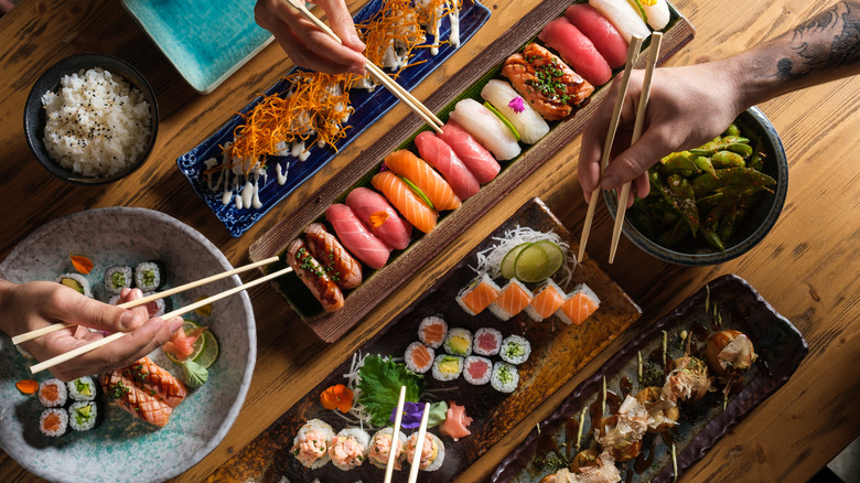 hands with chopsticks over sushi platters