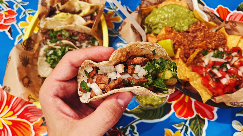 hand holding taco over colorful table set with nachos