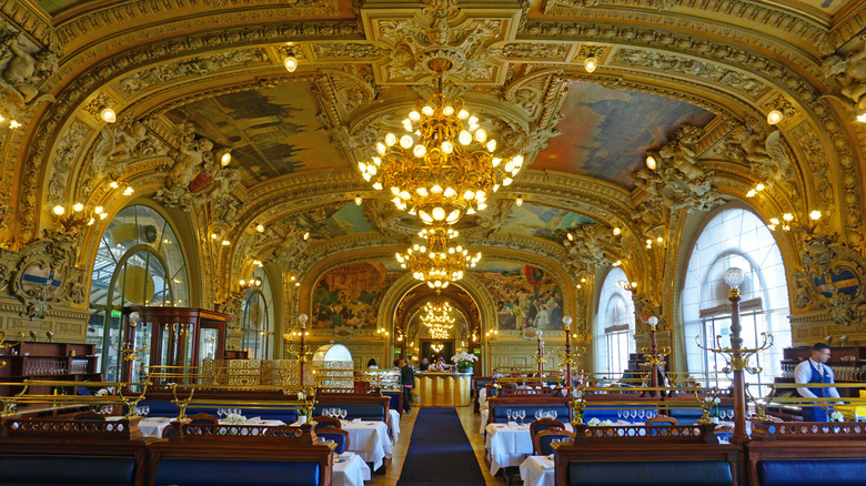 Interior of Le Train Bleu restaurant, with gilded walls, chandeliers, and colorful murals dating to 1900