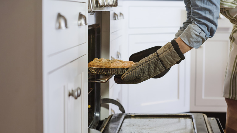 A person removes a pie from the oven in a home kitchen.