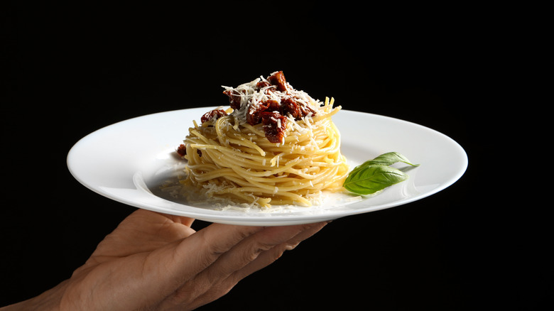 Person holding a white plate of spaghetti