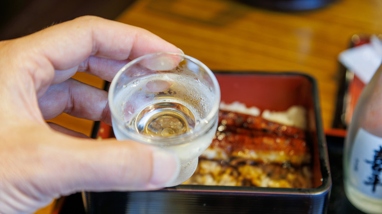 hand holding glass of sake over plate