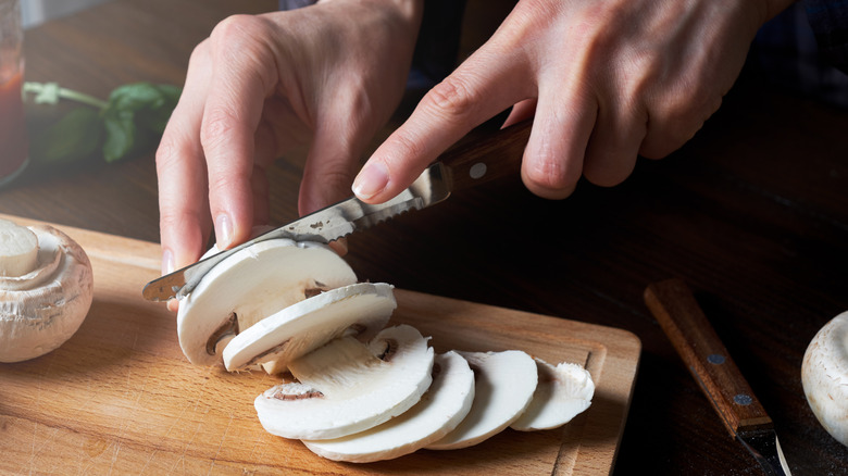 Hand slicing white mushroom with serrated knife