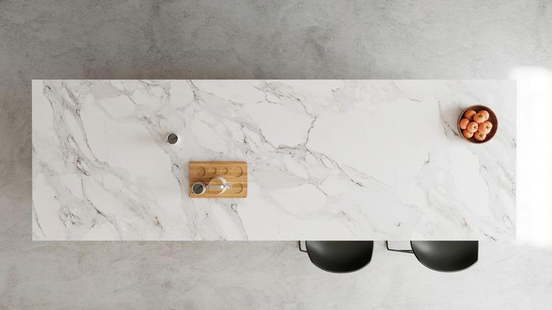 Overhead view of a marble kitchen island with two chairs and a bowl of oranges