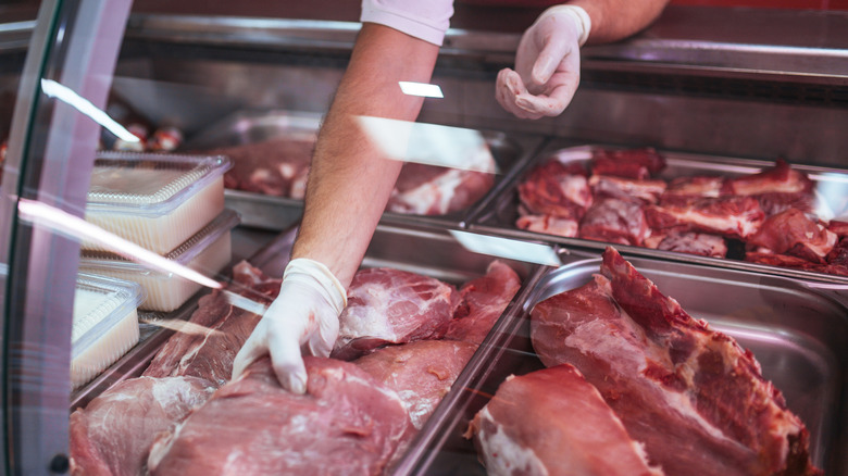 Butcher handles meat in a glass case.