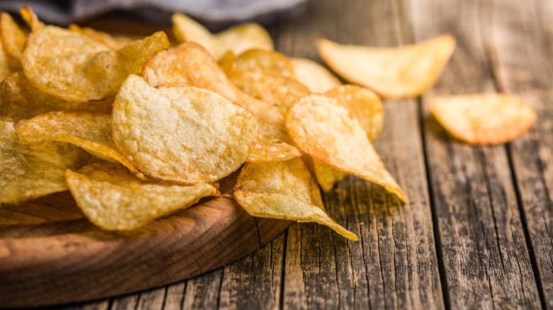 A pile of potato chips is spilling off a board onto a wood table.