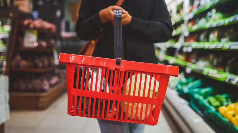 Woman with red hand basket grocery shopping