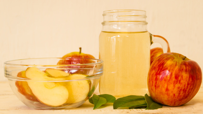 Mug of apple cider vinegar surrounded by apples