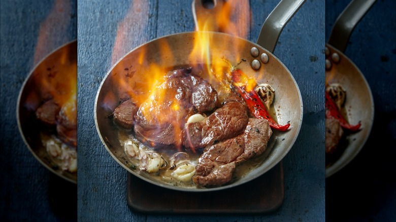 Steak flambeing in silver pan with chili, garlic, and onions