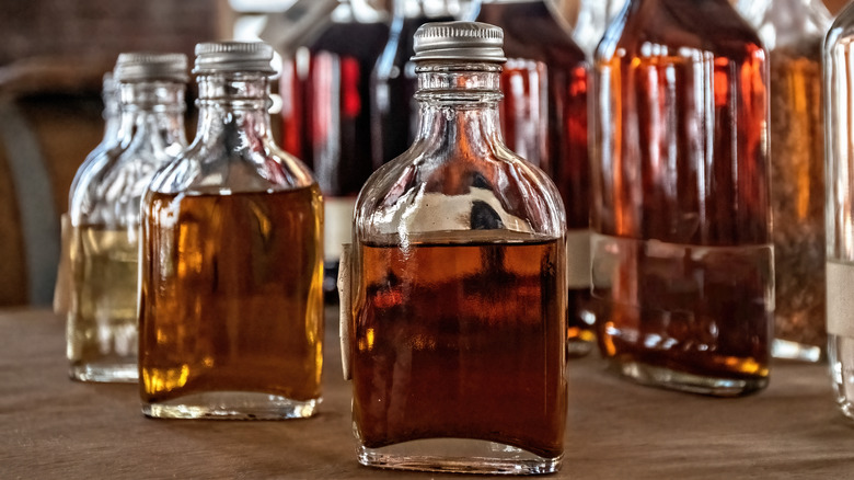 Several unlabeled bottles of brown liquor in a rustic setting.